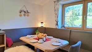 A dining area with a wooden table set for two, a cushioned bench, and a window with a view of greenery. - Beautiful private villa for 4 people with TV and terrace (Wildschönau)