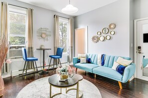 Un salon avec un canapé bleu, deux fauteuils bleus, une table basse ronde et une porte blanche.
