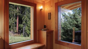 A wooden cabin interior with a bench under a window, a clock, and a small cabinet.