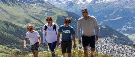 Un grupo de personas se encuentra en un sendero pedregoso en la montaña, con vistas a montañas nevadas y un valle.