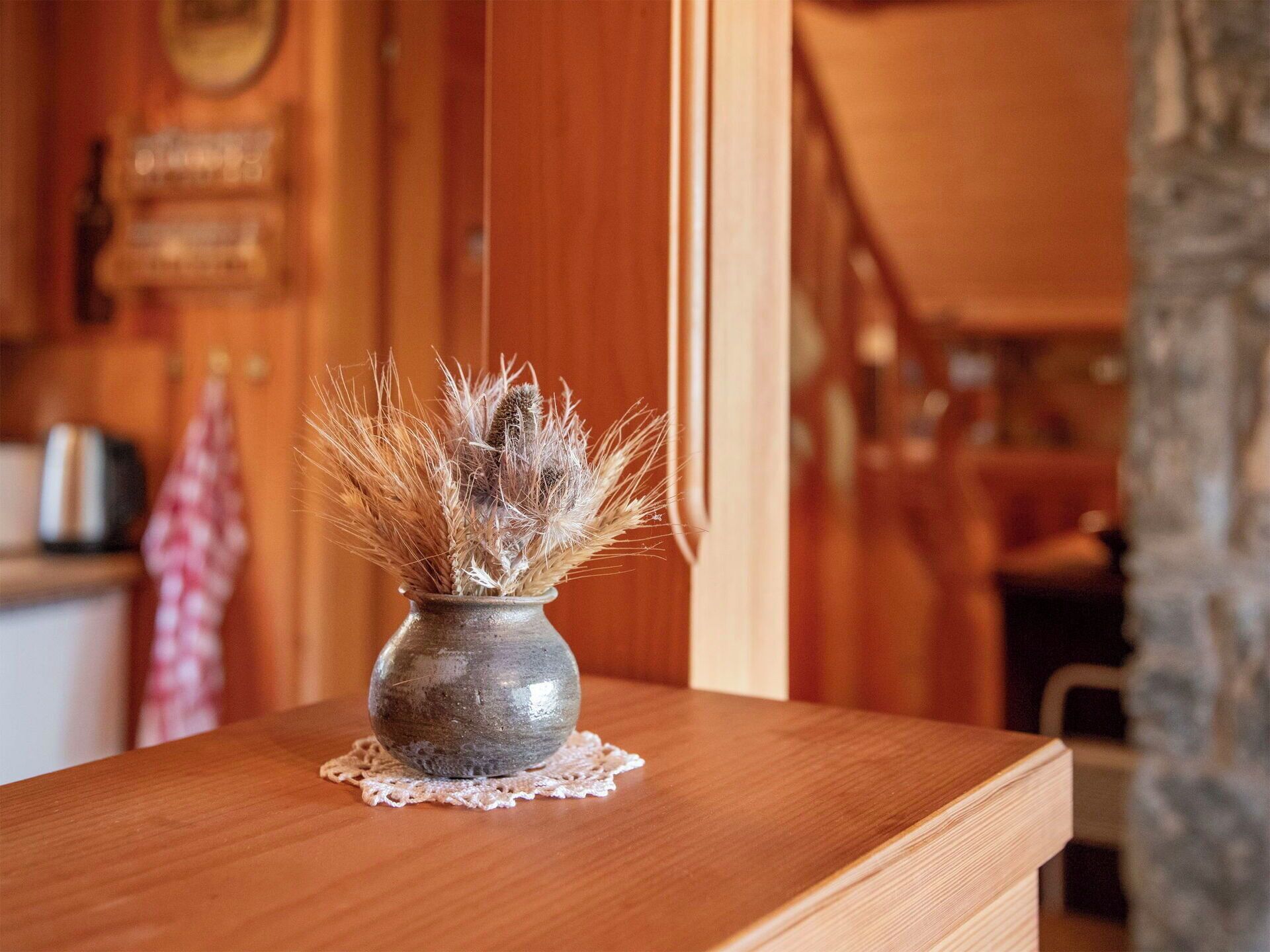 A rustic wooden table with a vase of dried plants on a doily.