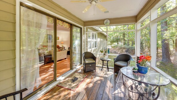 A covered porch with a ceiling fan, wicker chairs, a glass table, and a view of the outdoors.