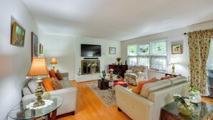 A living room with a sofa, armchairs, a glass coffee table, and a fireplace.