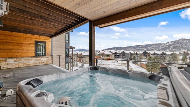Un jacuzzi en una terraza de madera con vistas a casas nevadas y montañas.