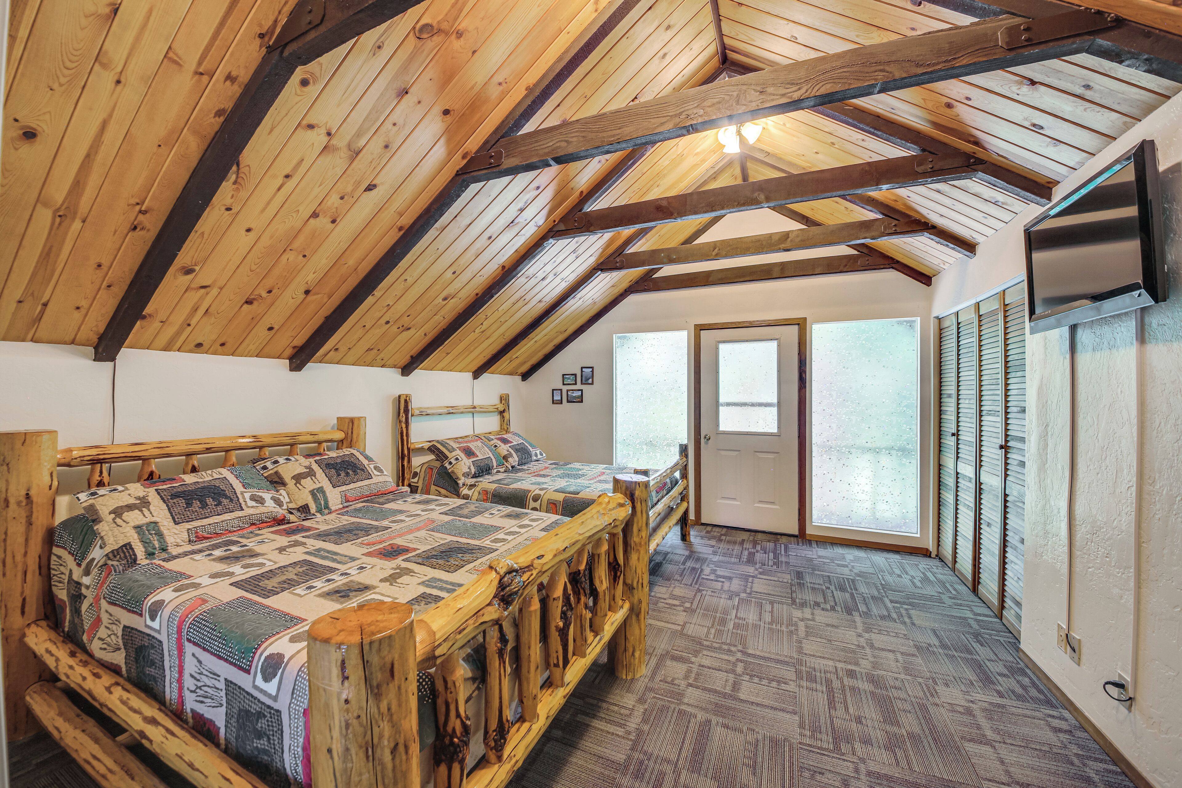 Ein Zimmer mit schrägverdeckter Holzbalkendecke, einem hölzernen Bett mit gemusterten Betttextilien und einem Teppichboden.