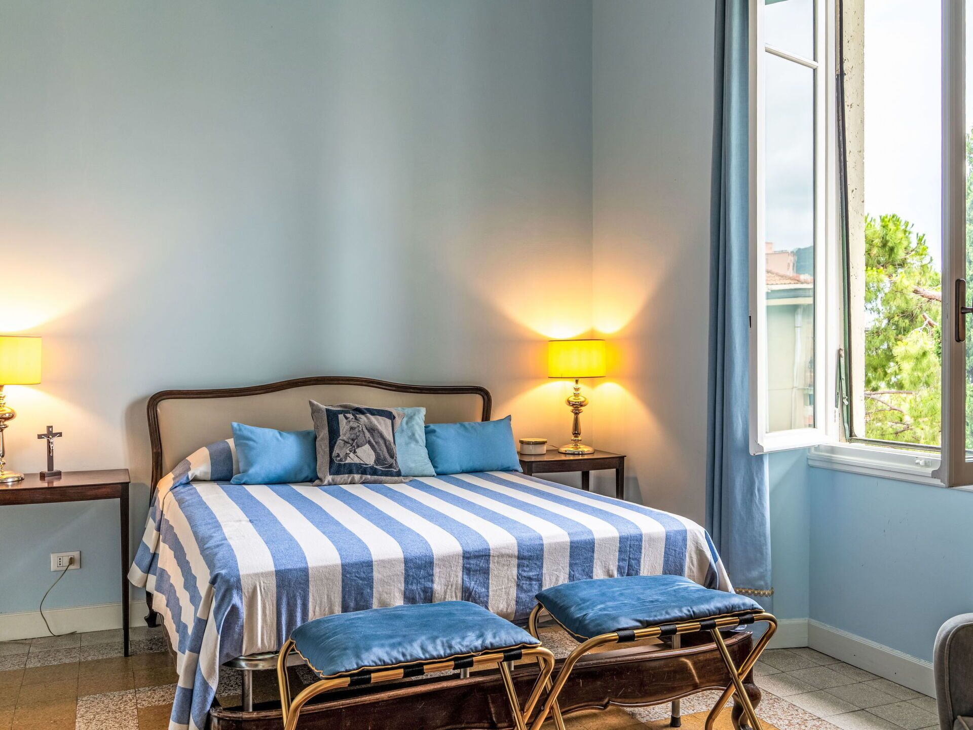 A bedroom with a bed, two bedside tables, a window, and a view of greenery outside.