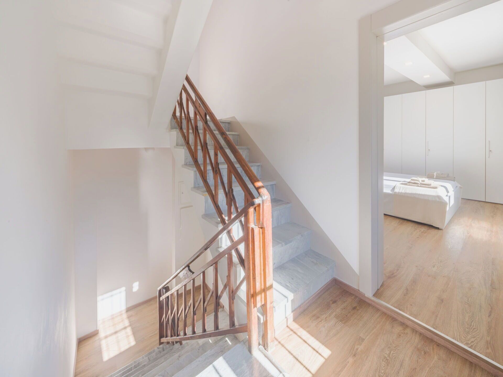 A staircase with wooden railings leading to a bedroom with a bed and a wardrobe.