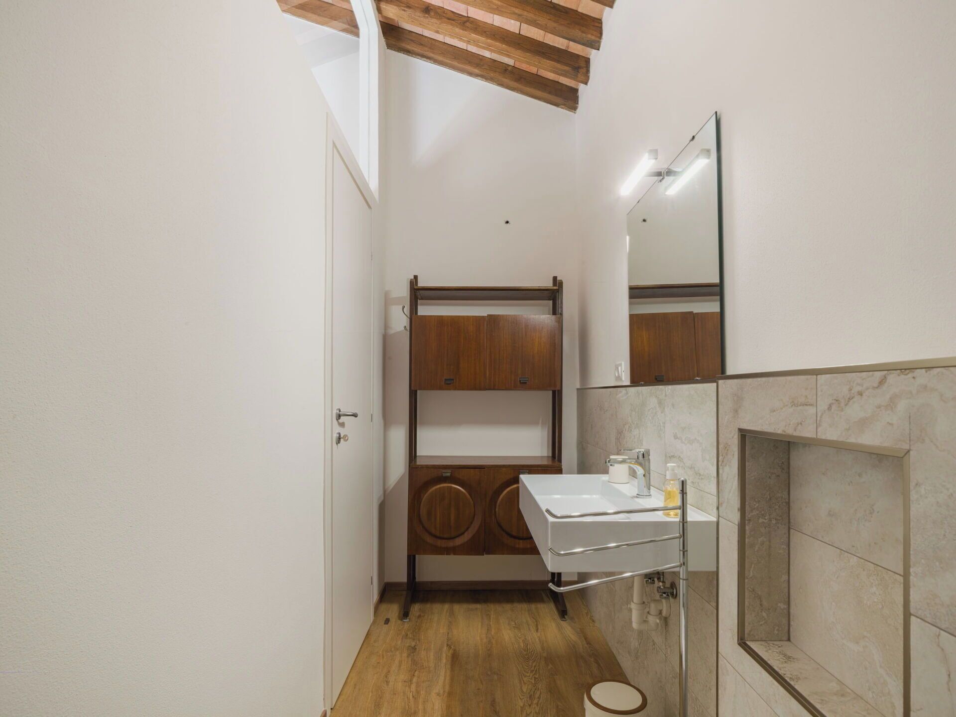 A compact bathroom with a wooden vanity, a white sink, and a mirror.