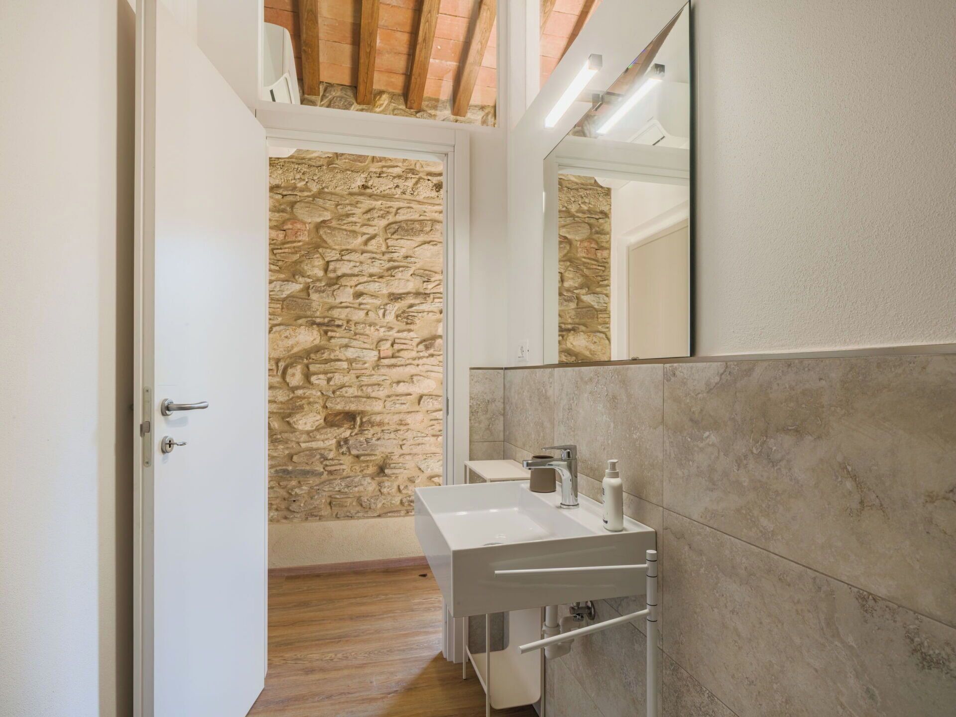 A modern bathroom with a stone wall, a white sink, and a mirror.