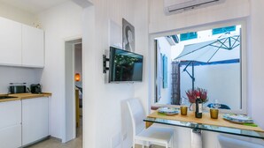 Uma cozinha moderna com armários brancos, uma mesa de jantar de vidro e uma TV fixada na parede.