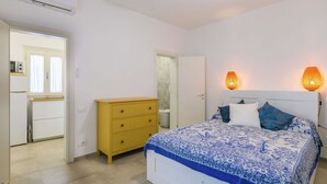 Quarto com cama, penteadeira, ar condicionado, ventilador de teto e porta para um banheiro.
