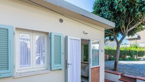 Um edifício de dois andares com fachada bege, porta de vidro deslizante e pequena área de tijolos que leva a um alpendre coberto.