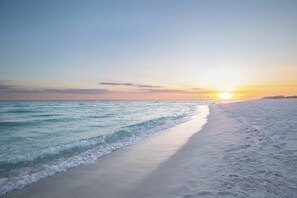 Una playa con cielo despejado y el sol poniéndose sobre el océano.