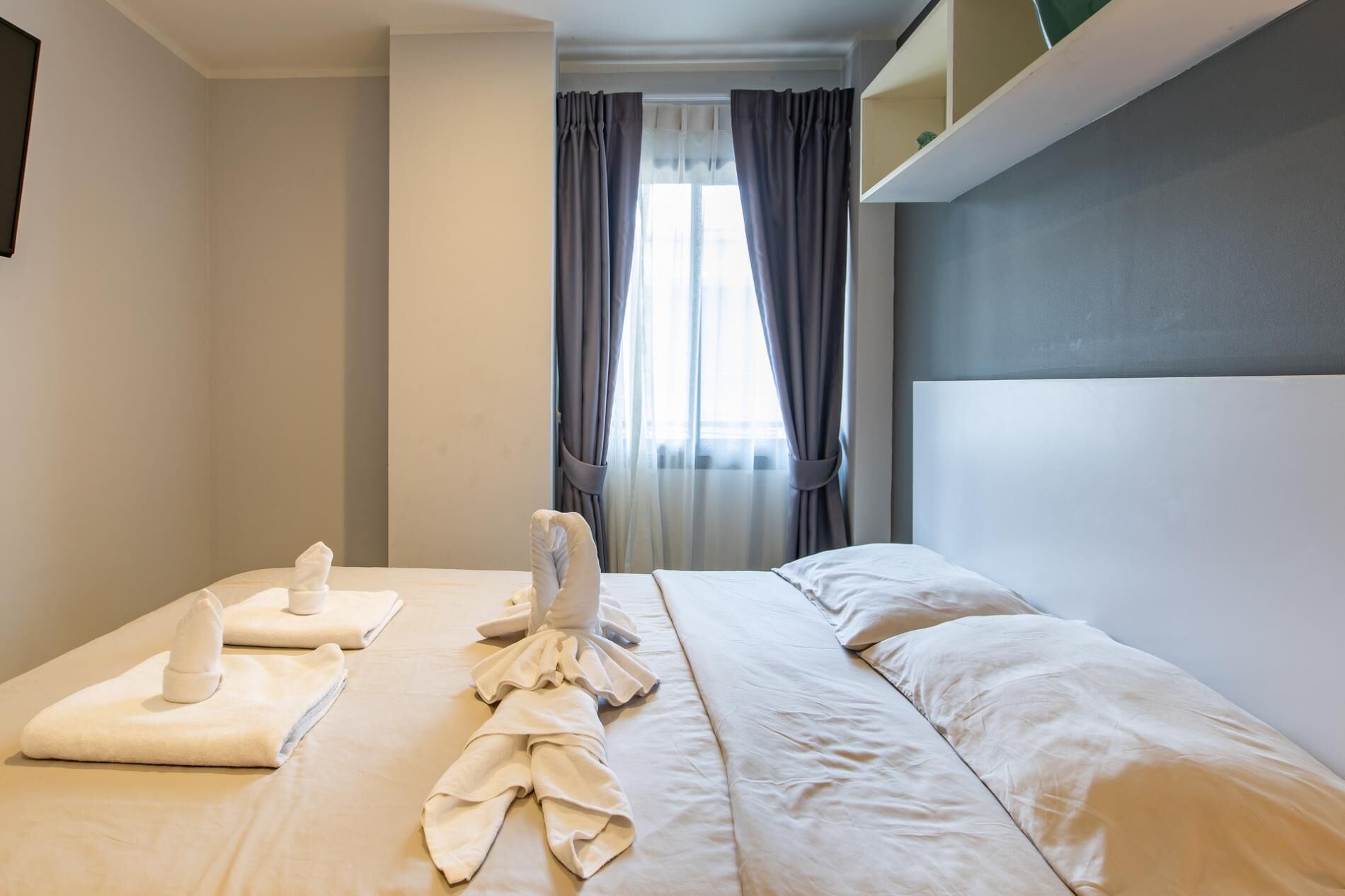 Ett hotellrum med en väl bäddad säng, ett litet bord med handdukar och ett fönster med gardiner.
