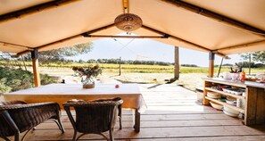 An outdoor dining area with a table and chairs under a canopy, overlooking a vineyard.