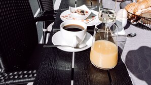 Un espacio exterior para comer con sillas y mesas negras, una variedad de platos, bebidas y una cesta de pan.
