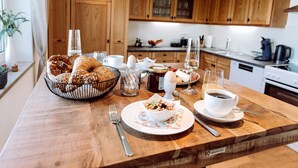 Un desayuno con pan, huevos y café sobre una mesa de madera en una cocina con alacenas de madera.