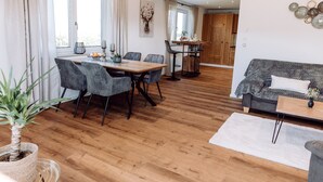 Una sala de estar moderna con comedor, suelo de madera y un sofá gris.