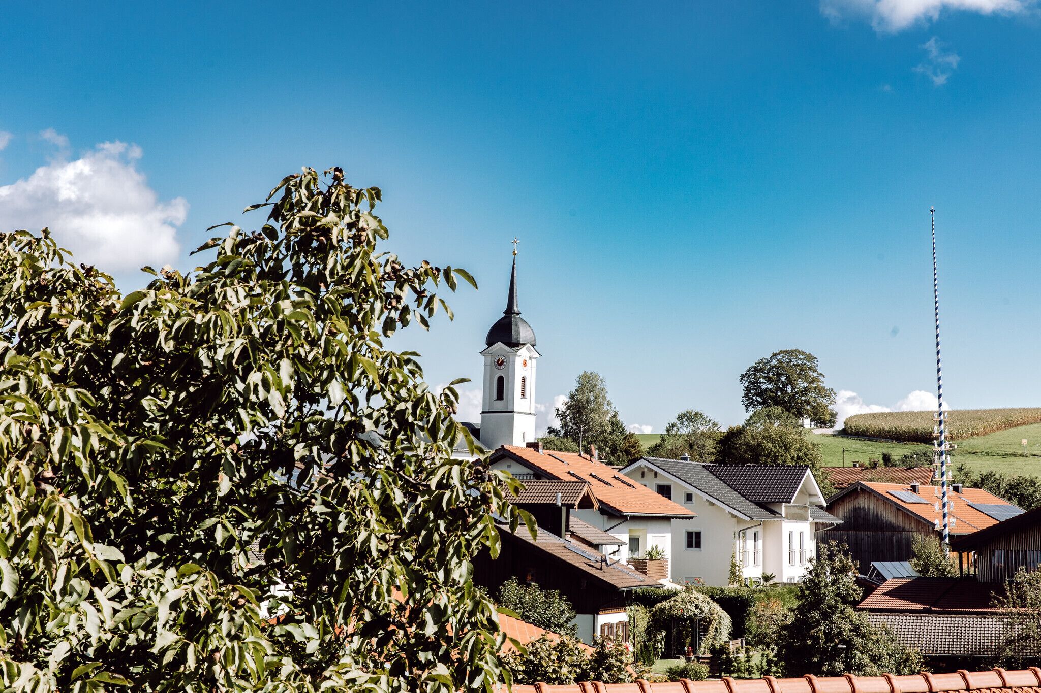A village with traditional houses, a church with a bell tower, and a clear blue sky.