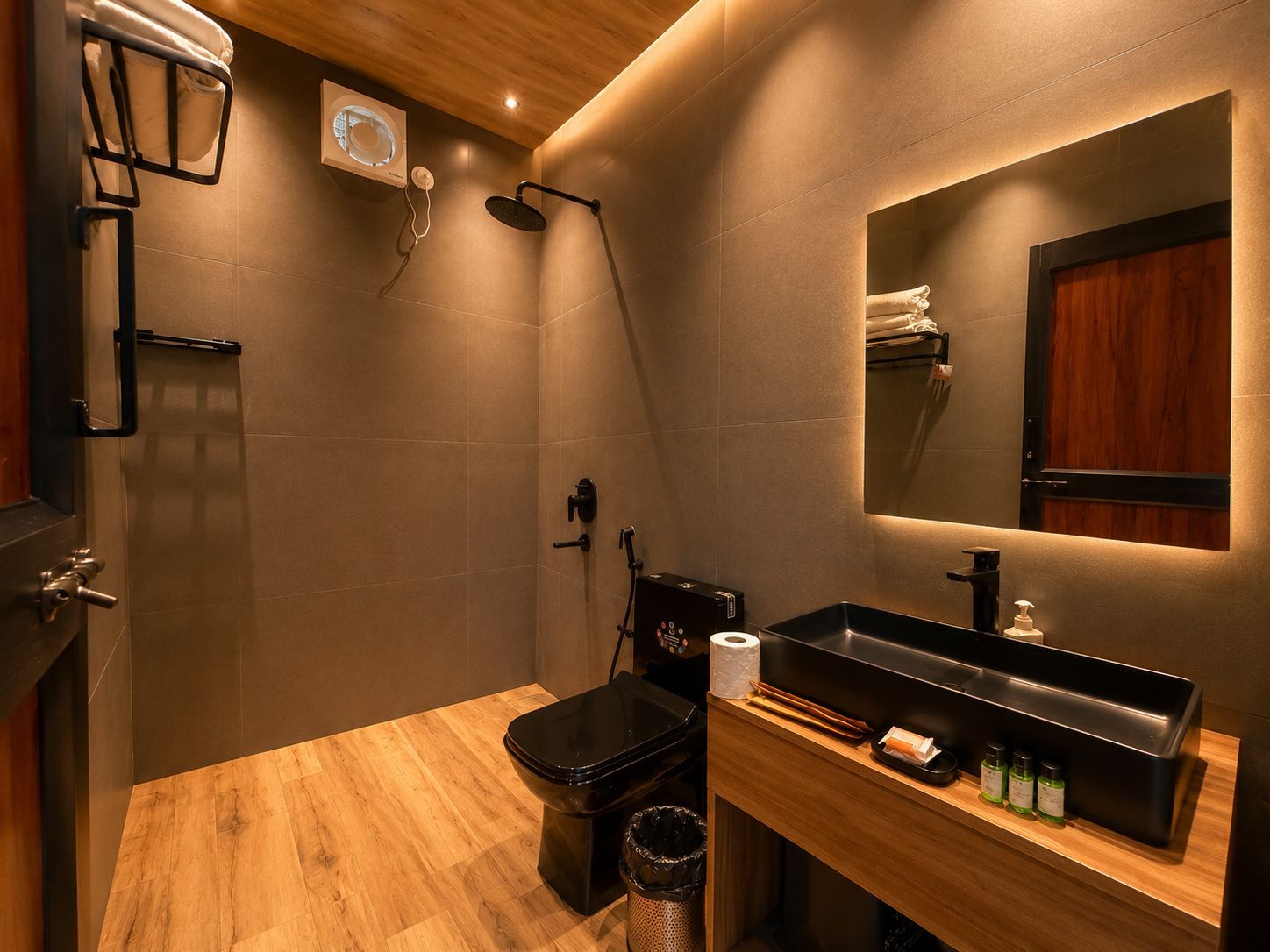 Une salle de bain moderne avec un plancher en bois, des toilettes noires, un lavabo avec un miroir et un espace douche.