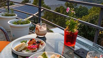 A table set with food and drinks on a balcony overlooking a mountainous landscape.