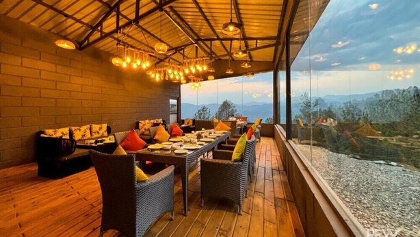 Ein Restaurant mit einem langen Esstisch, Korbstühlen und Blick auf die Berge durch große Fenster.