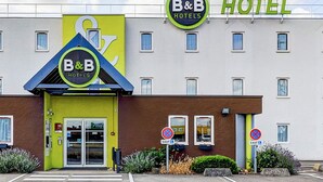 Un hotel tipo B&B con una fachada amarillo brillante, un logotipo azul y verde, y un letrero que indica que no hay estacionamiento.