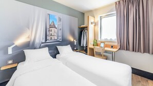 Habitación de hotel con dos camas, un escritorio, un armario y una ventana con cortinas.