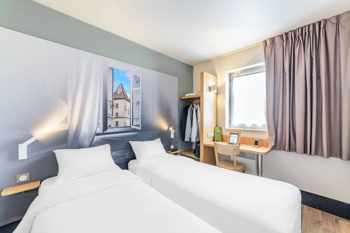 Une chambre d’hôtel avec deux lits, un bureau, une armoire et une fenêtre avec des rideaux.