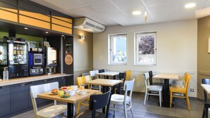Un café con mesas y sillas, una barra con una máquina de café y un ventanal con vistas.