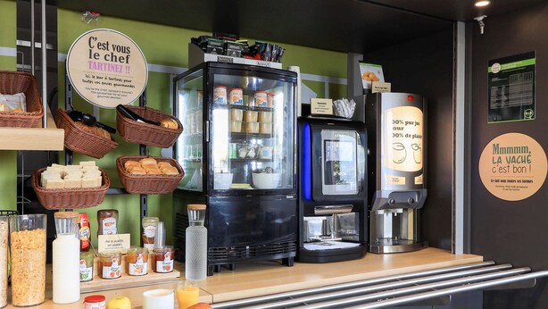 Una barra de desayuno con refrigerador, cafetera y diversas opciones de comida.