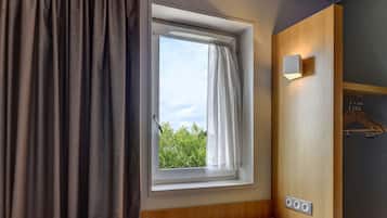 A room with a window, a curtain, a wooden bench, a wall-mounted light, and a power outlet.