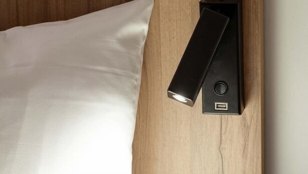 Una cama con un almohadón blanco y una mesita de noche negra con puerto USB.