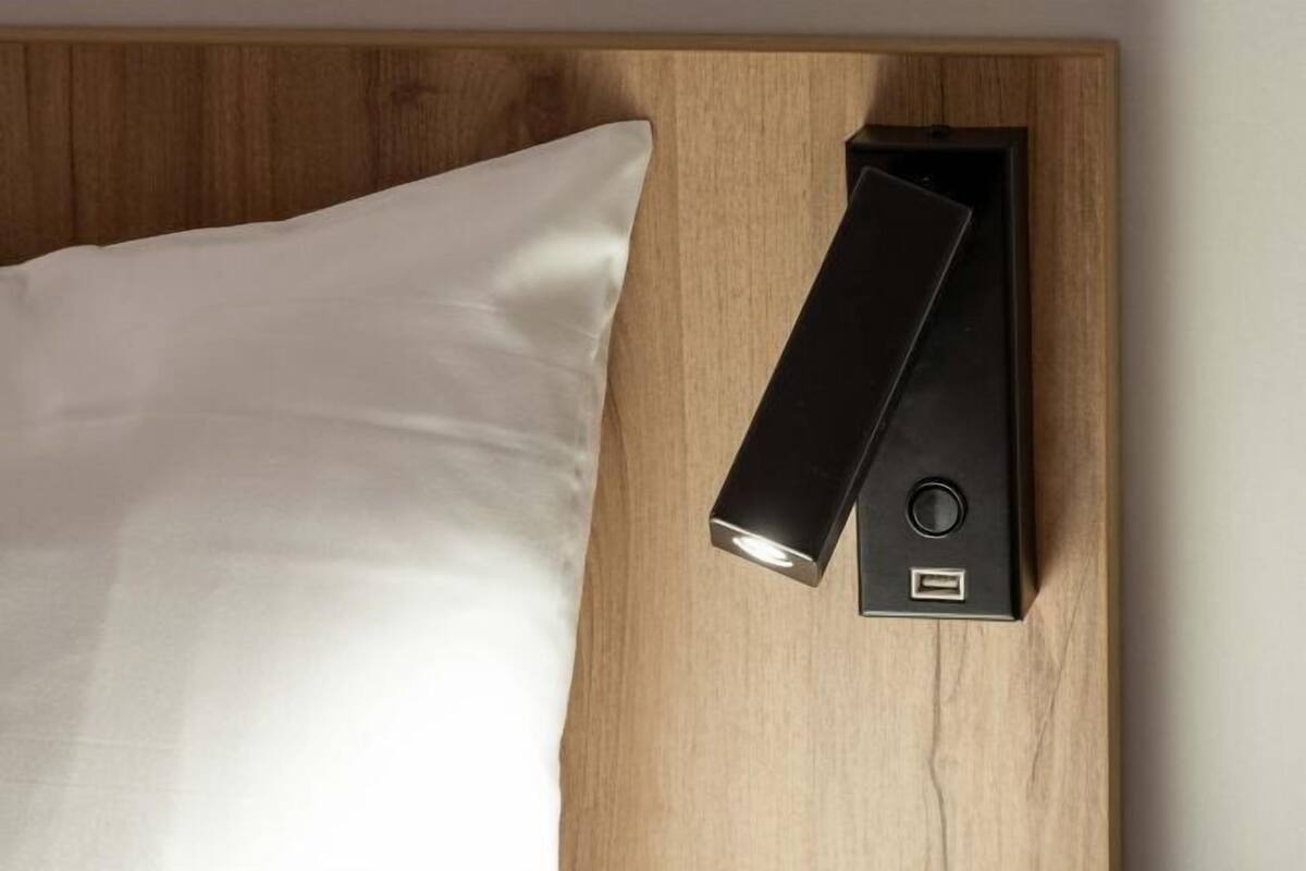 Un lit avec un oreiller blanc et une table de chevet noire dotée d’un port USB.