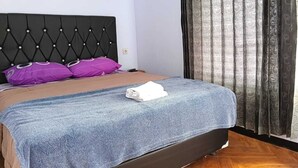 Een net opgemaakt bed met een blauwe deken, een zwart hoofdbord en twee paarse kussens.