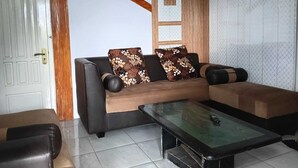 Een woonkamer met een bank, twee fauteuils, een glazen salontafel en een houten trap.