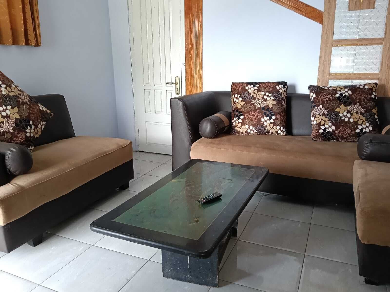 Una sala de estar con un juego de sofá, una mesa de centro de vidrio y una puerta al fondo.