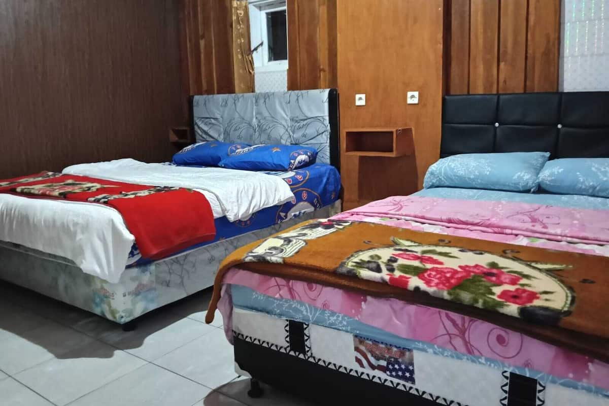 Two beds with different bedding, a wooden headboard, a small bedside table, and a window with a view.