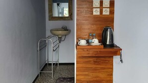 Een badkamer met een wastafel, spiegel en houten wastafelmeubel, inclusief waterkoker en kopjes.