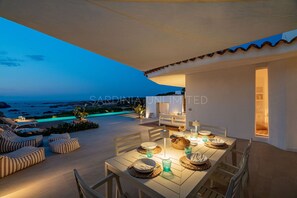 Un espace extérieur aménagé pour les repas, avec vue sur la mer, une piscine et un coin salon abrité.