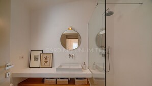 Un bany modern amb un lavabo blanc, un mirall gran i una dutxa amb envàs de vidre.