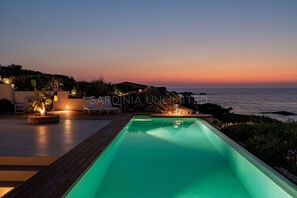 Un espace aménagé au bord de la piscine, offrant une vue sur le coucher du soleil, avec des chaises longues et une sculpture de cactus bien éclairée.