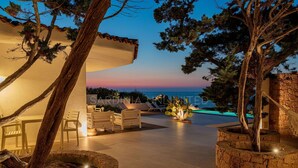 A well-lit outdoor area with a pool, lounge chairs, and a view of the sea at dusk. - Villa Janas Eterea - Sardinia Unlimited (Portobello Di Gallura)