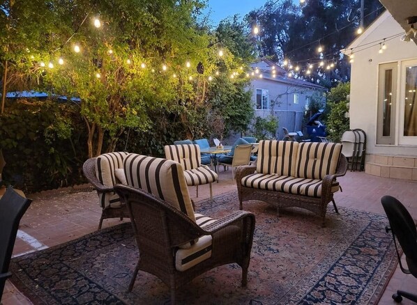 An outdoor patio area with wicker furniture, a patterned rug, and string lights.