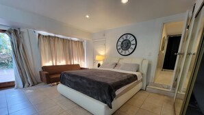 Quarto moderno com cama grande, sofá, relógio na parede e área de chuveiro.