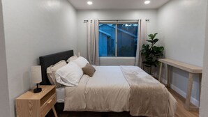 Een slaapkamer met een bed, nachtkastje, lamp en uitzicht.