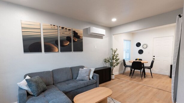 Een moderne woonkamer met een grijze bank, een houten salontafel en een eethoek met een kleine tafel en stoelen.