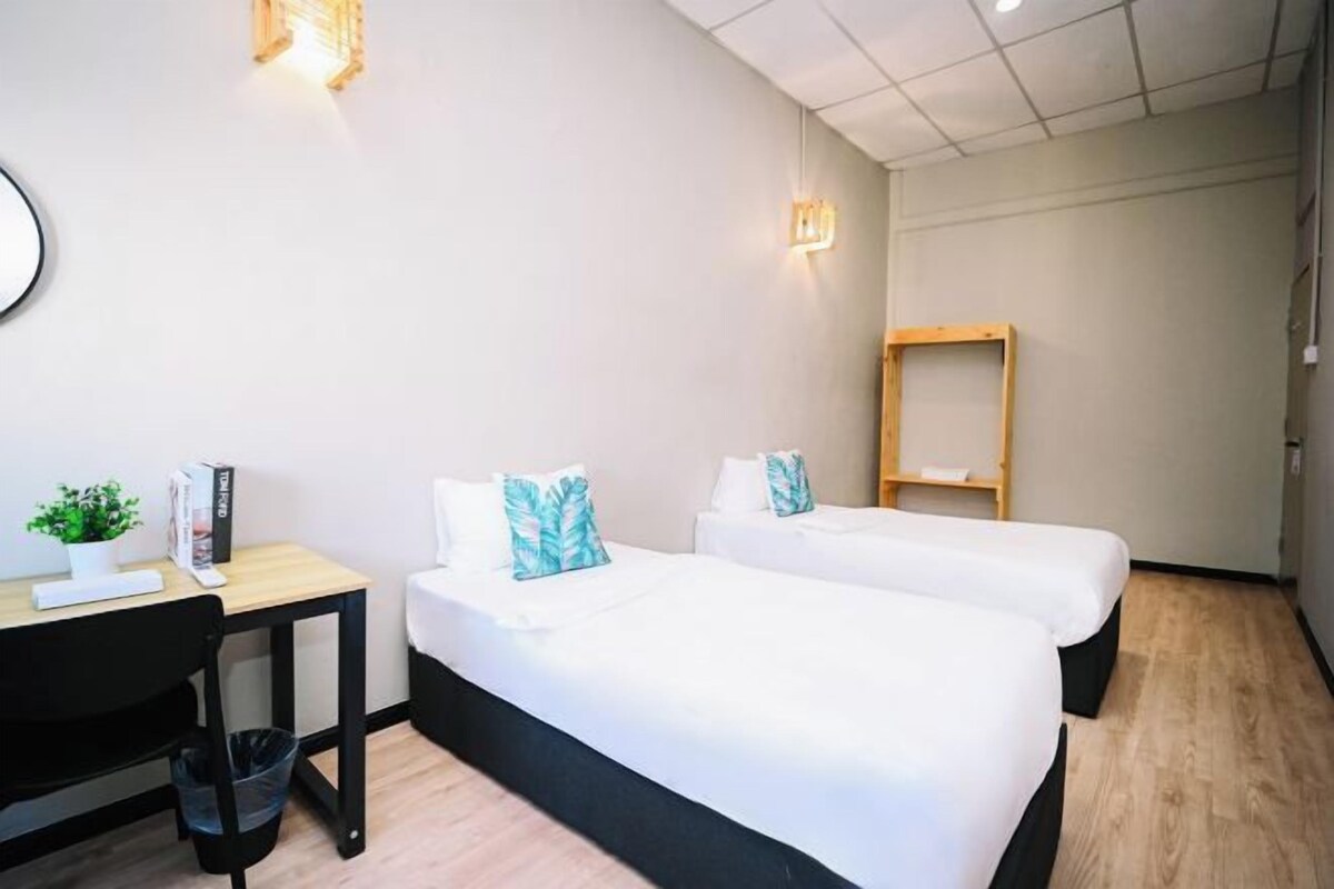 A hotel room with two beds, a desk, a chair, a small table, and a trash bin.