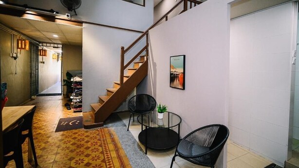A staircase leading to a second floor, a dining area with a table and chairs, and a small seating area with a plant. - Swing & Pillows at 87 Chulia St (George Town)