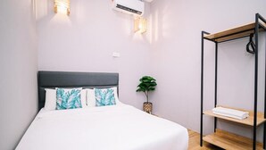 A neatly made bed with white and blue pillows, a small potted plant, and a wooden shelf with a towel. - Swing & Pillows at 87 Chulia St (George Town)